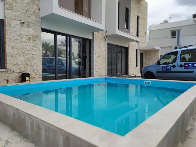 Piscine rectangulaire turquoise devant un bâtiment moderne et un van bleu