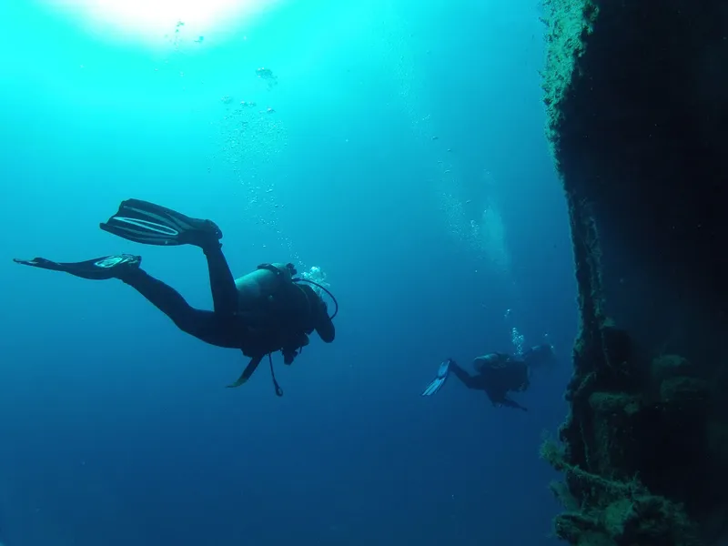 Deux plongeurs explorent un épave sous-marine dans une eau bleue