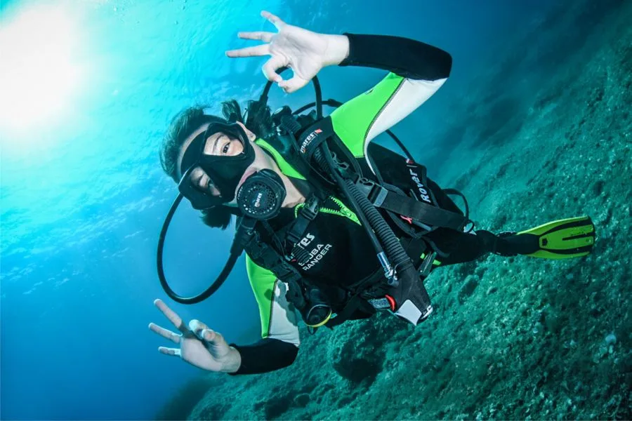 Plongeuse souriante avec signe de la victoire sous l'eau bleue