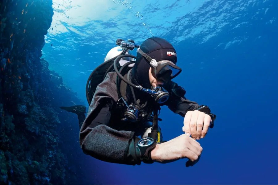 Plongeur vérifiant son ordinateur de plongée en milieu aquatique bleu