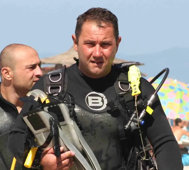 Deux plongeurs en combinaison, équipés, regardent vers l'avant sur une plage