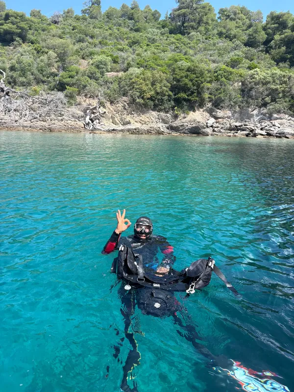 Plongeur en surface avec signe OK, eau turquoise, côte rocheuse