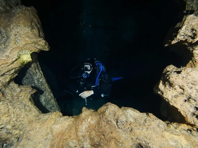 Plongeur explorant une grotte sous-marine sombre et rocheuse avec prudence