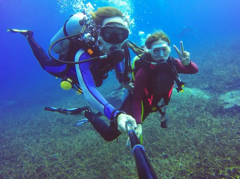 Deux plongeuses souriantes font un signe de la main sous l'eau