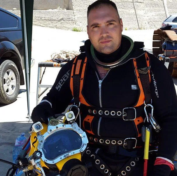 Plongeur souriant en combinaison, casque et équipement complet près d'une voiture