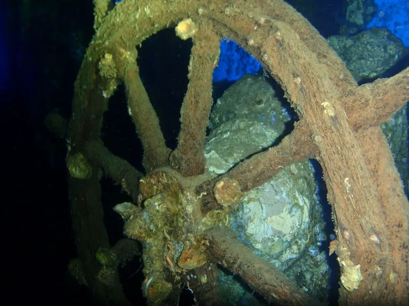Epave rouillée et rocheuse sous l'eau, lumière bleutée, exploration marine
