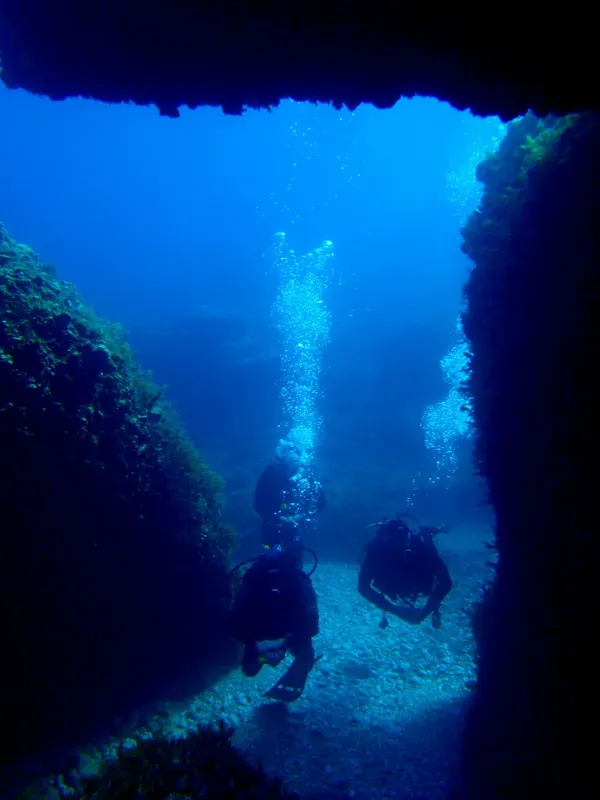 Deux plongeurs explorent une grotte sous-marine, bulles remontant vers la surface