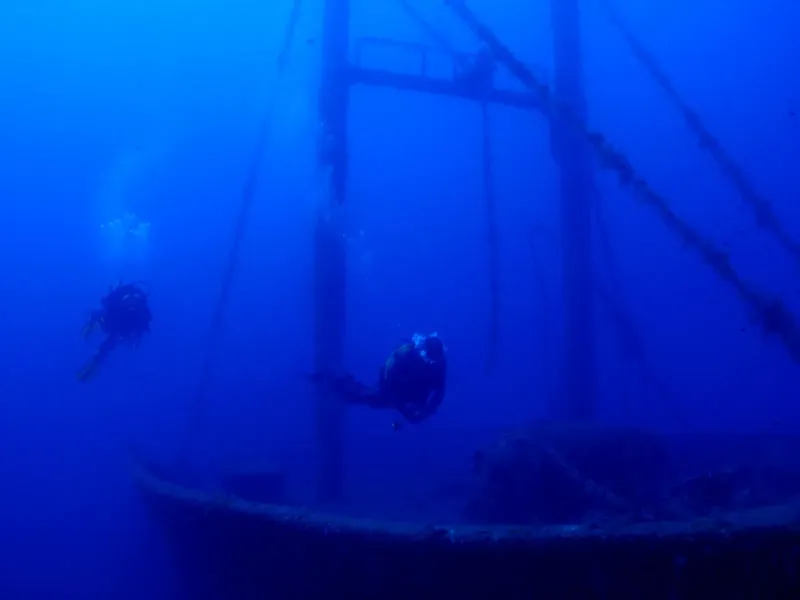 Deux plongeurs explorent une épave métallique sous l'eau bleue