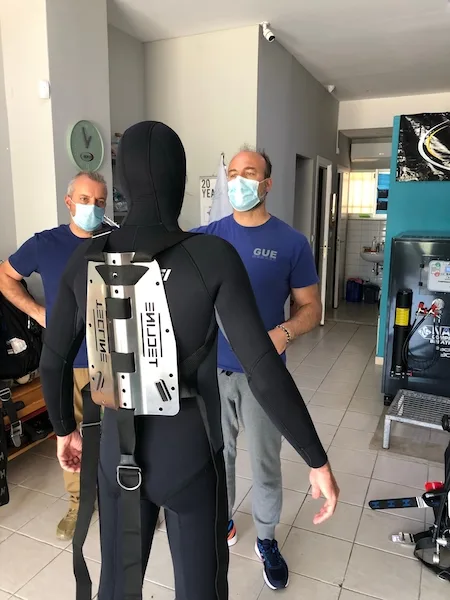 Deux hommes et une personne en combinaison de plongée dans un local