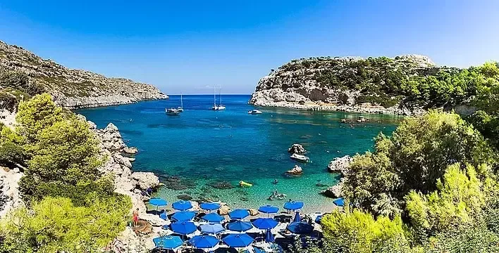 Crique turquoise avec bateaux, parasols et quelques baigneurs détendus