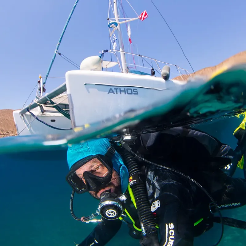 Plongeur équipé nage sous un bateau à voile en mer