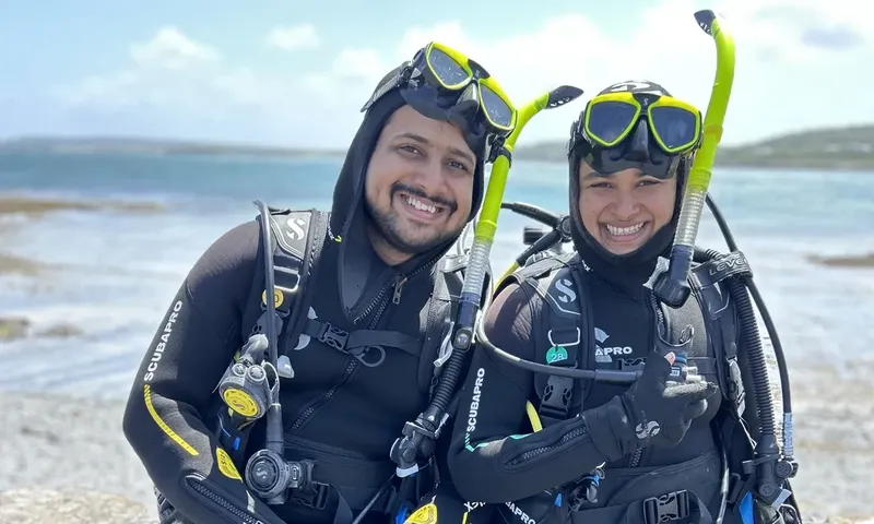 Deux plongeurs souriants en combinaison, équipés, sur une plage ensoleillée
