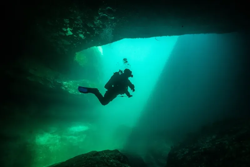 Plongeur explore une grotte sous-marine éclairée par un rayon de soleil