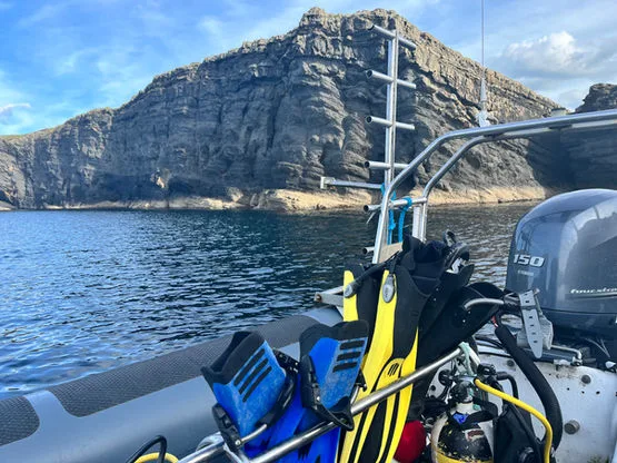 Bateau de plongée avec palmes et bouteilles devant une côte rocheuse