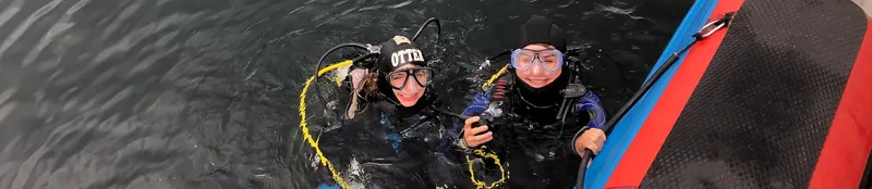 Deux plongeurs en combinaison noire sourient à bord d'un bateau