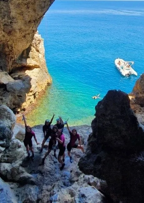 Groupe de personnes souriantes sur des rochers surplombant une mer bleue