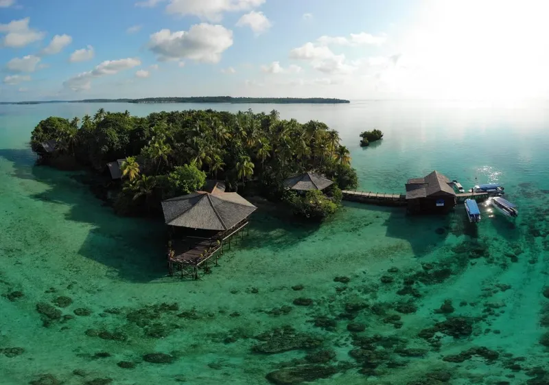 Île tropicale avec bâtiments sur pilotis et bateaux amarrés turquoise