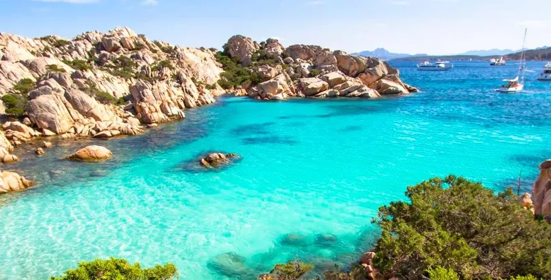 Cote rocheuse et mer turquoise avec quelques bateaux au loin