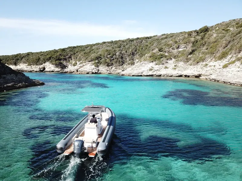 Bateau semi-rigide naviguant dans une crique aux eaux turquoise et claires