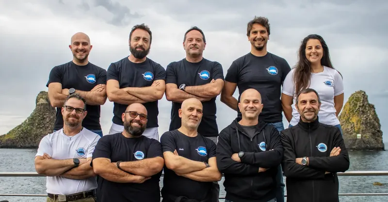 Groupe de personnes souriantes, bras croisés, devant un paysage marin