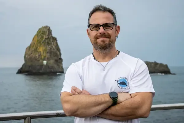 Homme souriant avec des lunettes, bras croisés, devant la mer