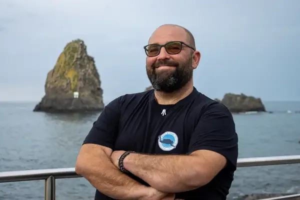 Homme souriant sur un bateau avec une île rocheuse en arrière-plan