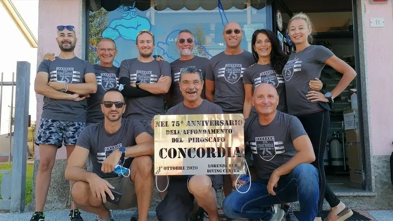 Groupe de personnes souriantes devant le centre de plongée et un panneau commémoratif