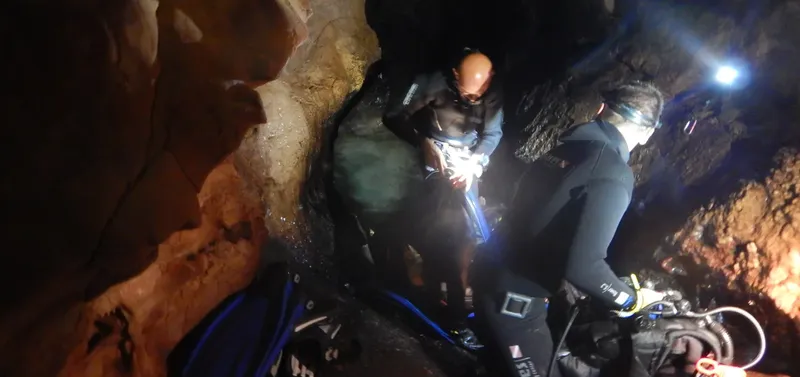 Deux plongeurs explorent une grotte sous-marine sombre et rocheuse
