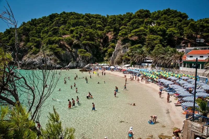 Plage ensoleillée avec baigneurs et parasols, bâtiments en arrière-plan