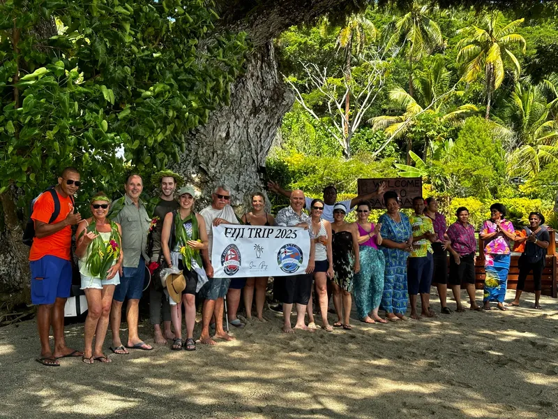 Groupe de personnes souriantes posant avec une bannière Fiji Trip 2025