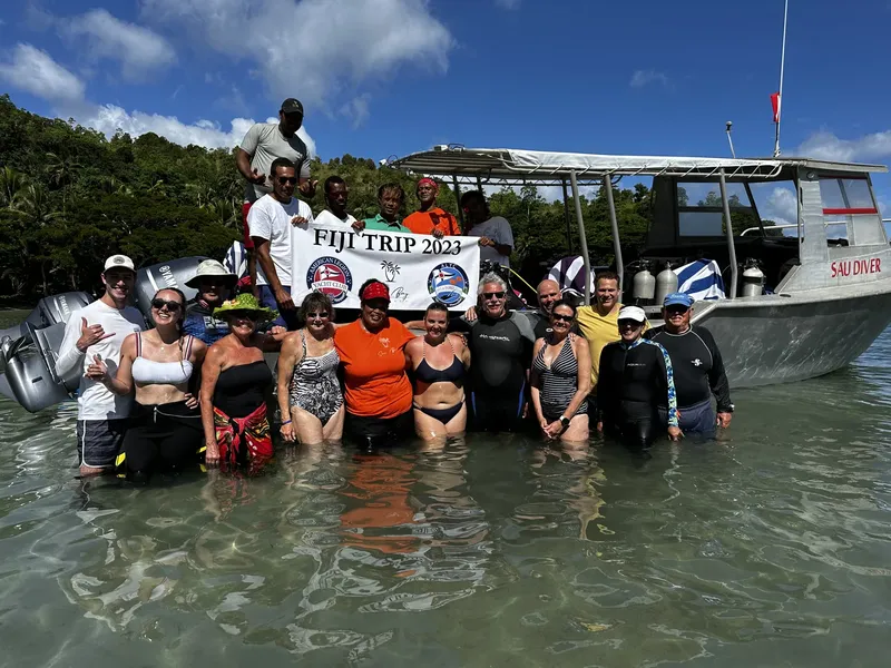 Groupe de plongeurs souriants devant un bateau avec une bannière Fiji