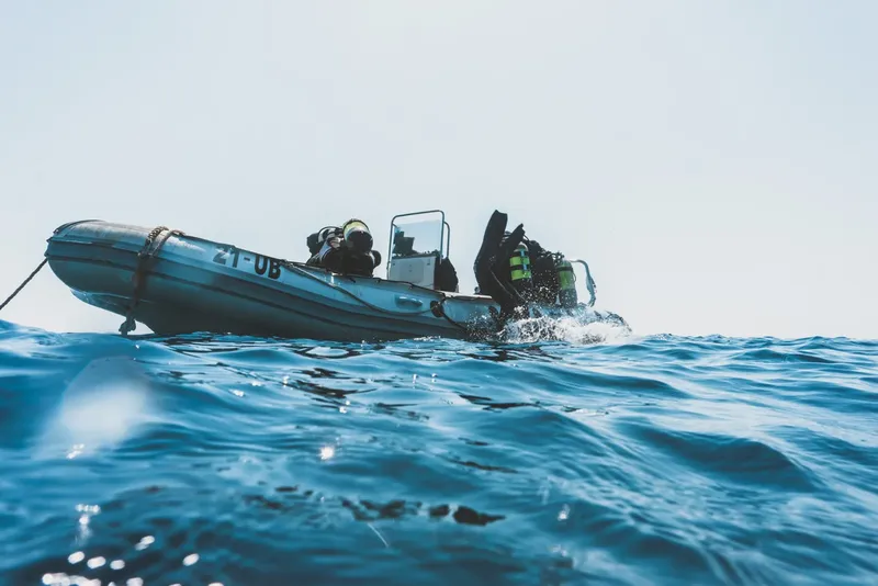 Plongeurs s'apprêtent à entrer dans l'eau depuis un bateau pneumatique bleu