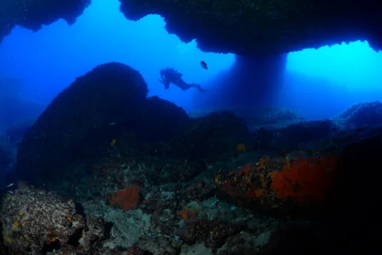 Plongeur explorant une grotte sous-marine avec lumière et roches