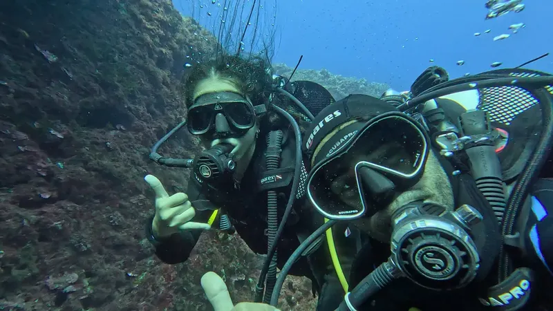 Plongeur souriant avec signe de la main sous l'eau rocheuse