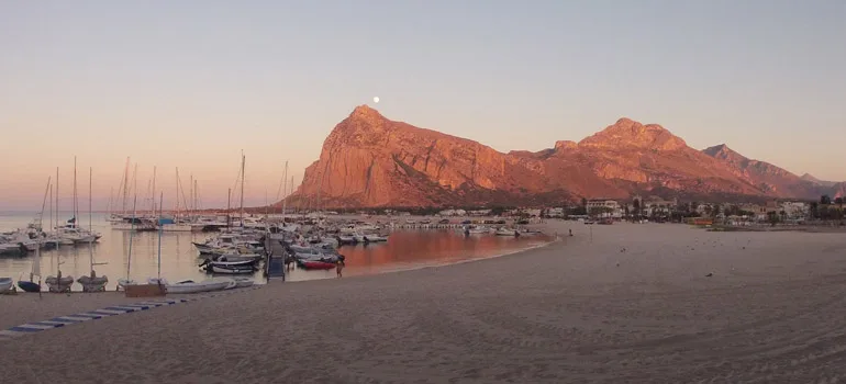 Plage, bateaux amarrés, montagnes en arrière-plan, ciel au coucher du soleil