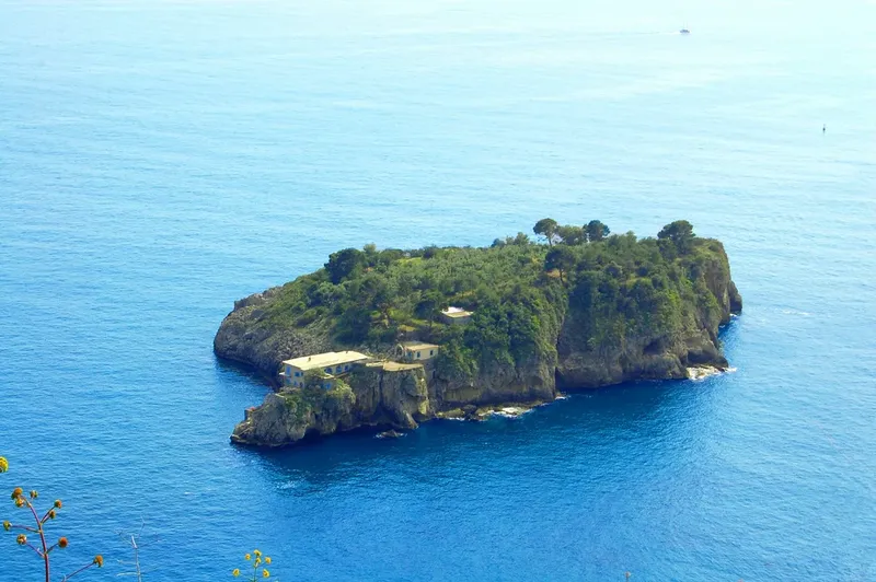 Île rocheuse couverte de végétation avec un bâtiment blanc en bord de mer