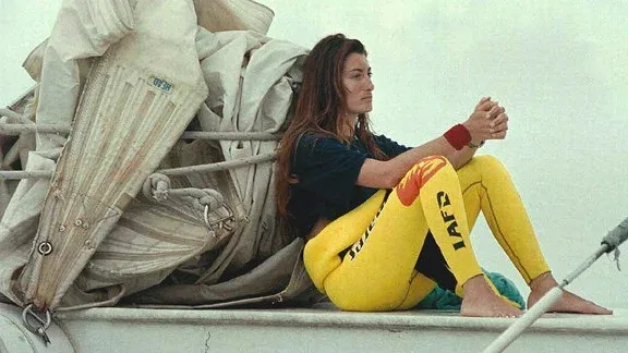 Femme assise sur un bateau, regardant au loin, combinaison jaune