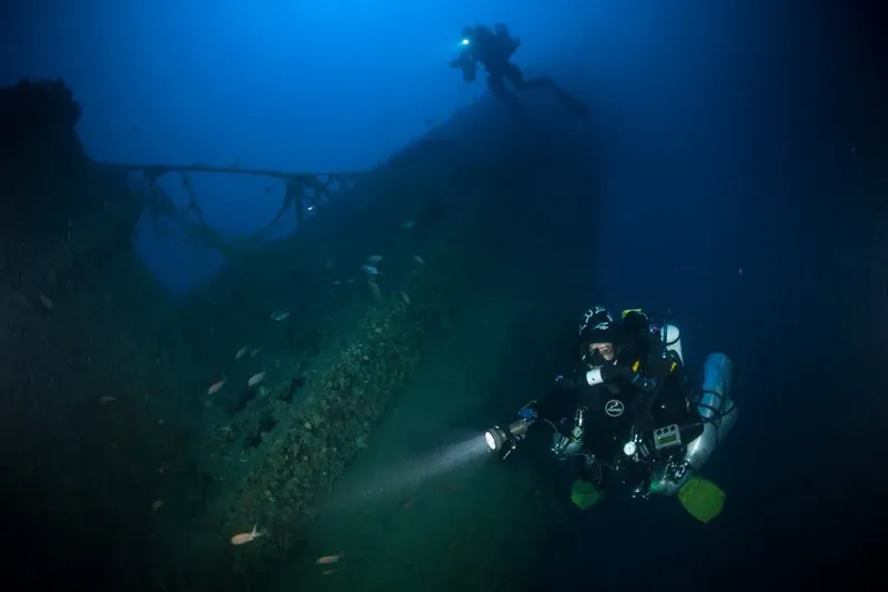 Deux plongeurs explorent une épave sous-marine dans l'eau bleue