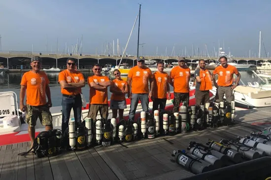 Groupe de plongeurs souriants posant avec des bouteilles sur un ponton