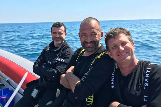 Trois plongeurs souriants sur un bateau en mer, équipés