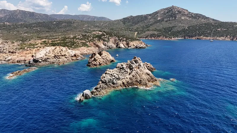 Côte rocheuse avec des îlots, mer bleue et quelques bateaux au large