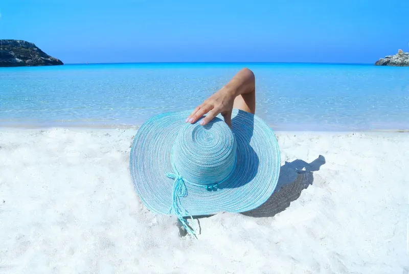 Main et chapeau de paille sur plage de sable blanc turquoise