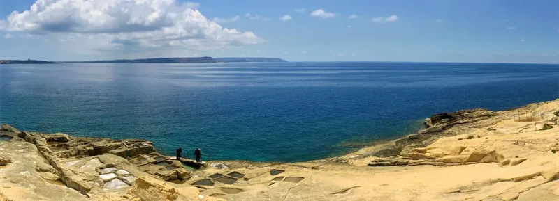 Deux personnes se tiennent sur des rochers face à la mer bleue