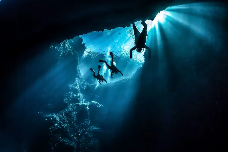 Trois plongeurs explorent une grotte sous-marine éclairée par le soleil