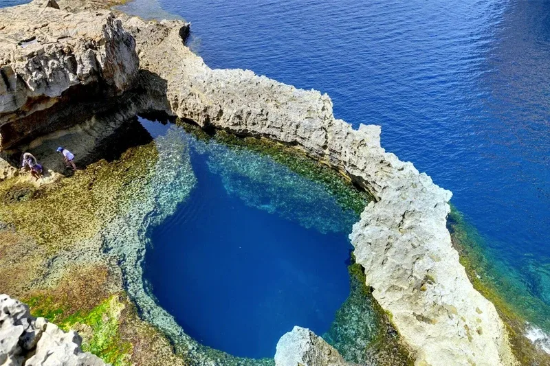 Personnes sur une falaise rocheuse surplombant une crique turquoise