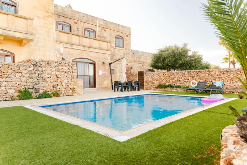 Piscine rectangulaire devant un bâtiment en pierre avec pelouse verte