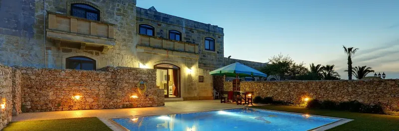 Bâtiment en pierre avec piscine éclairée et végétation luxuriante