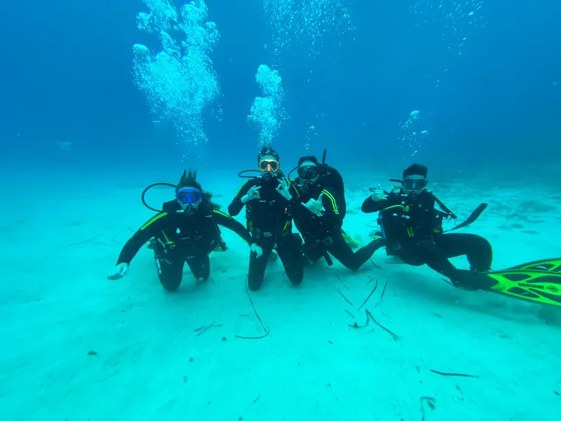 Quatre plongeurs souriants posent sur le fond sableux en mer