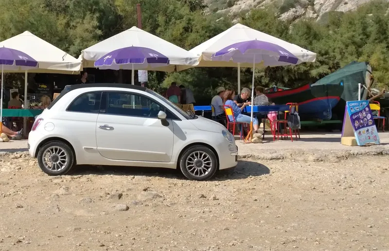 Terrasse de café avec des clients et une voiture blanche garée