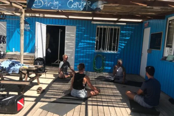 Quatre personnes assises sur des tapis devant un centre de plongée